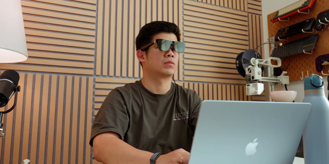 Pria memakai kacamata AR saat bekerja dengan laptop Macbook